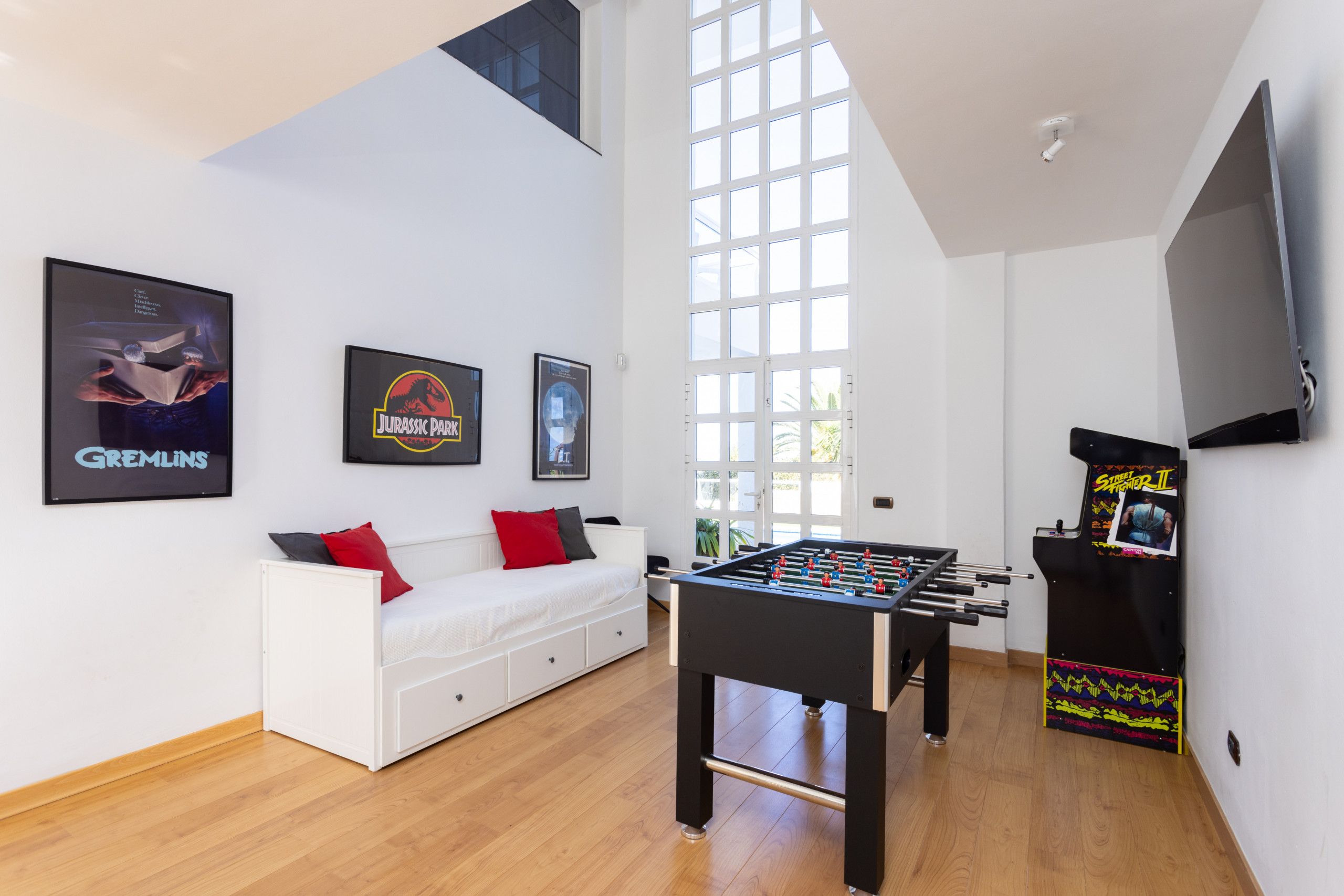 Uma sala de estar moderna com mesa de futebol, sofá branco e uma janela grande.