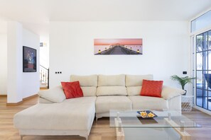 A modern living room with a beige sectional sofa, a glass coffee table, and a large window.