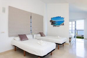A hotel room with two single beds, a large window, and a view of the sea.