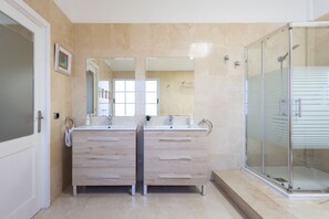A modern bathroom with two sinks, a large mirror, and a glass-enclosed shower.
