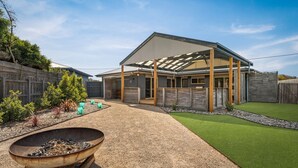 Ein modernes Haus mit überdachter Terrasse, einem Schotterweg und einem kleinen Garten mit Rasenmatte und Pflanzen.