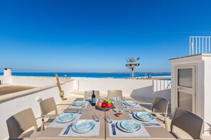 A table set for four with a view of the sea, a white building, and a lifeguard tower in the background. - 3185 Una Finestra sul Porto by Barbarhouse (Gallipoli)