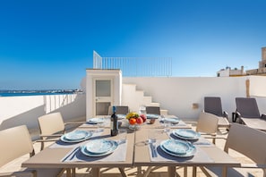 A rooftop dining area with tables set for four, a fruit bowl, and a bottle of wine. - 3185 Una Finestra sul Porto by Barbarhouse (Gallipoli)
