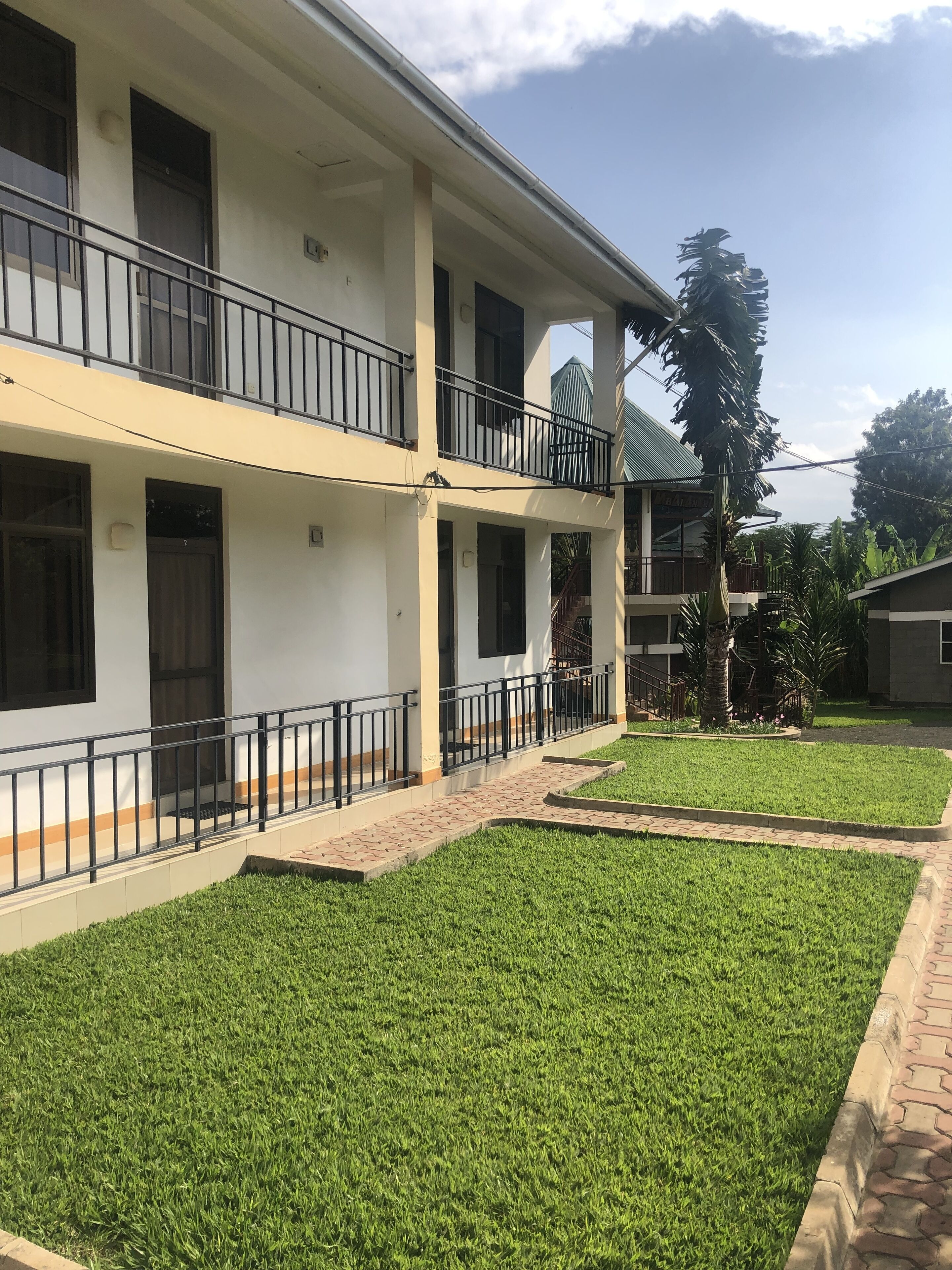 A two-story building with a flat roof, a balcony on the upper floor, and a well-maintained lawn in front.