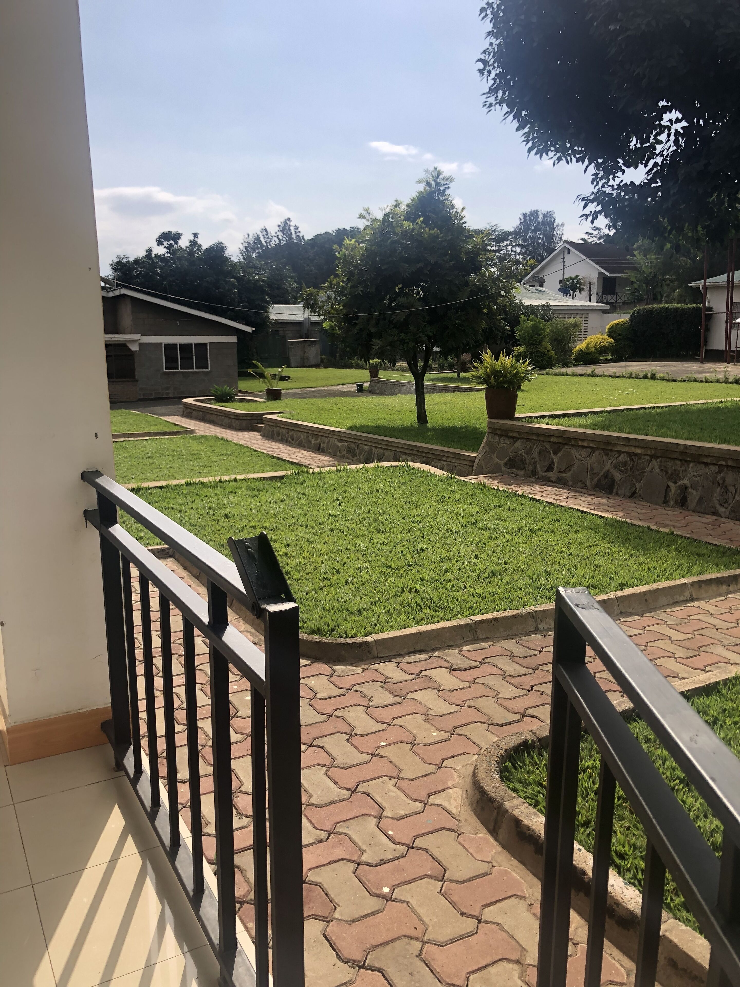 A balcony with a view of a well-maintained lawn, stone pathways, and a building in the background.