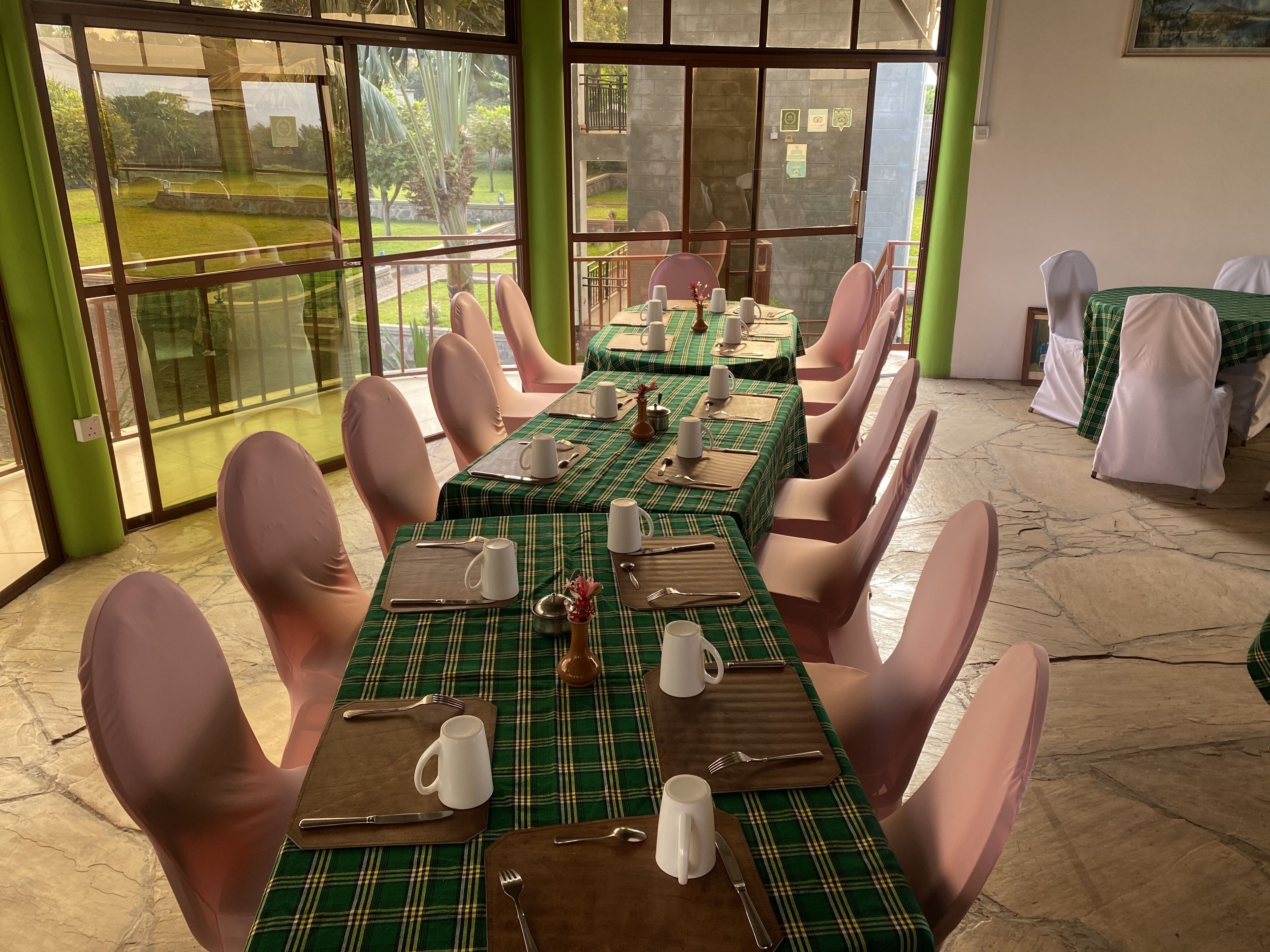 A dining area with tables set for four, each with a green plaid tablecloth, white plates, and pink chairs.