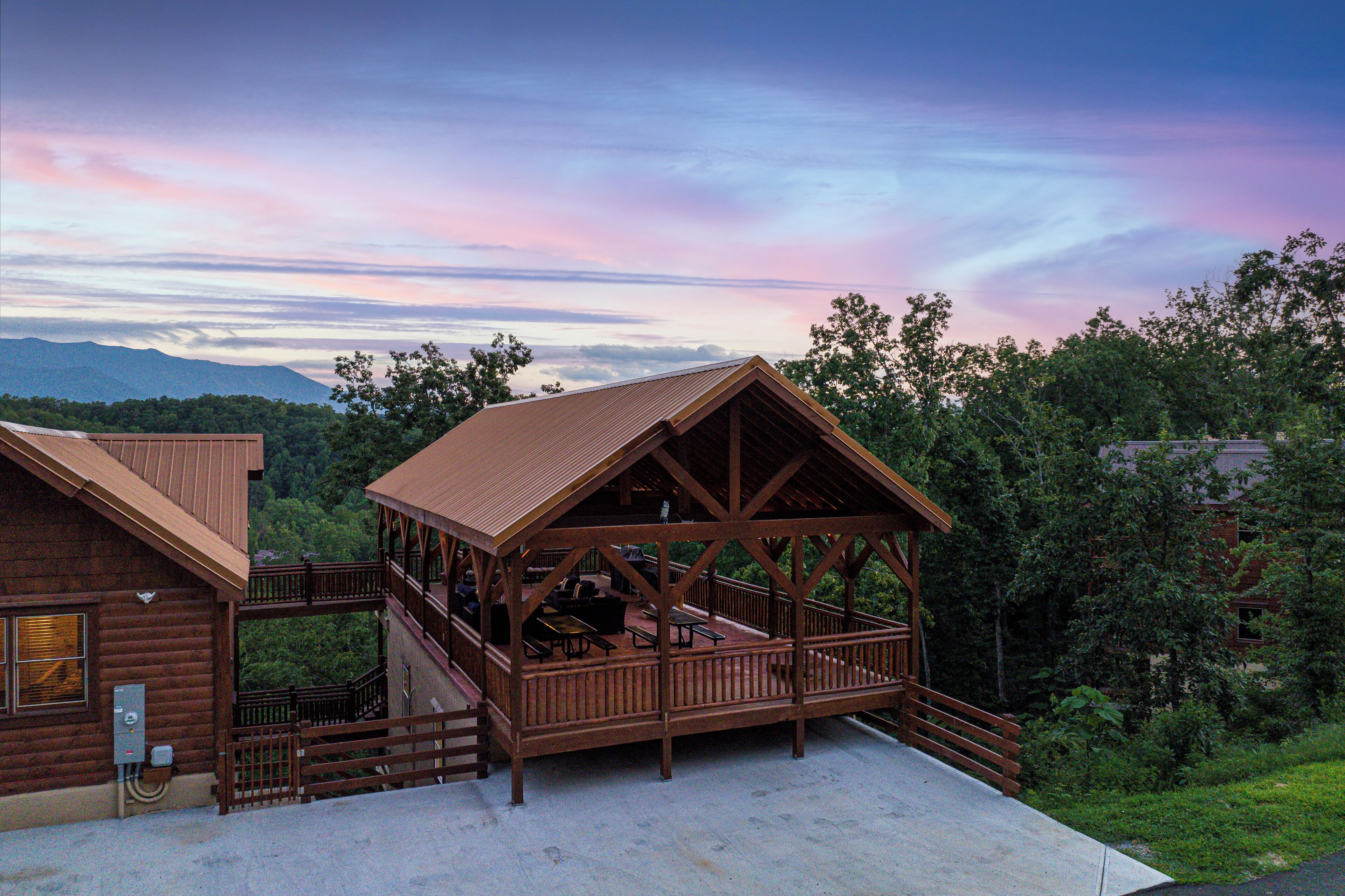 A wooden cabin with a balcony and a deck, surrounded by trees and mountains.