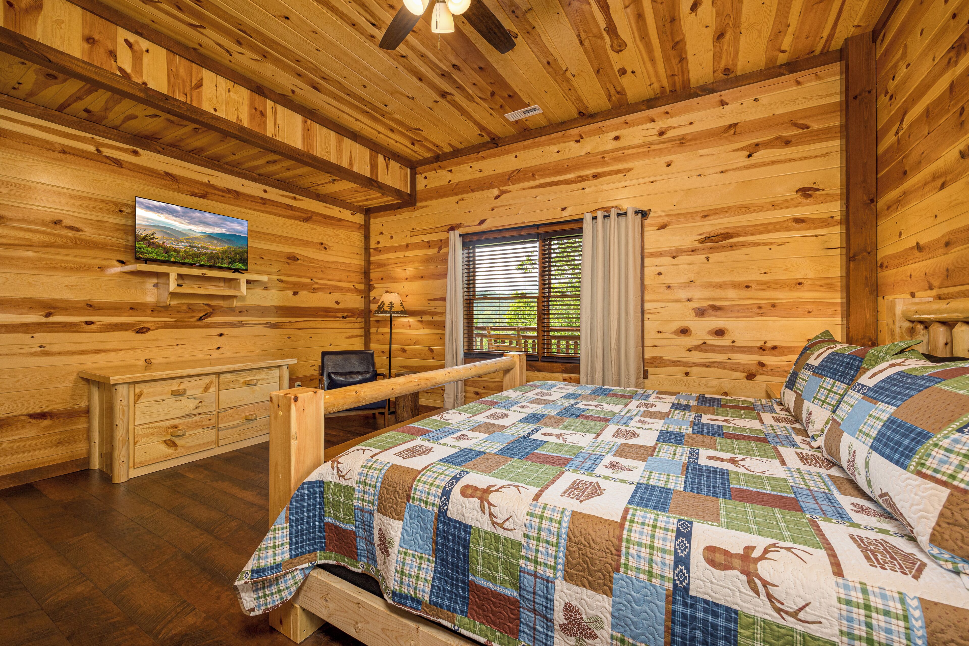 Una habitación de cabaña de madera con una cama, un escritorio y un televisor en la pared.