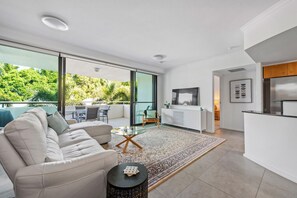 Relax in a spacious living area with a sofa, coffee table, and dining table, leading to an outdoor space surrounded by lush greenery.