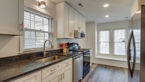 Una cocina moderna con armarios blancos, encimera de granito, electrodomésticos de acero inoxidable y una ventana con persianas.