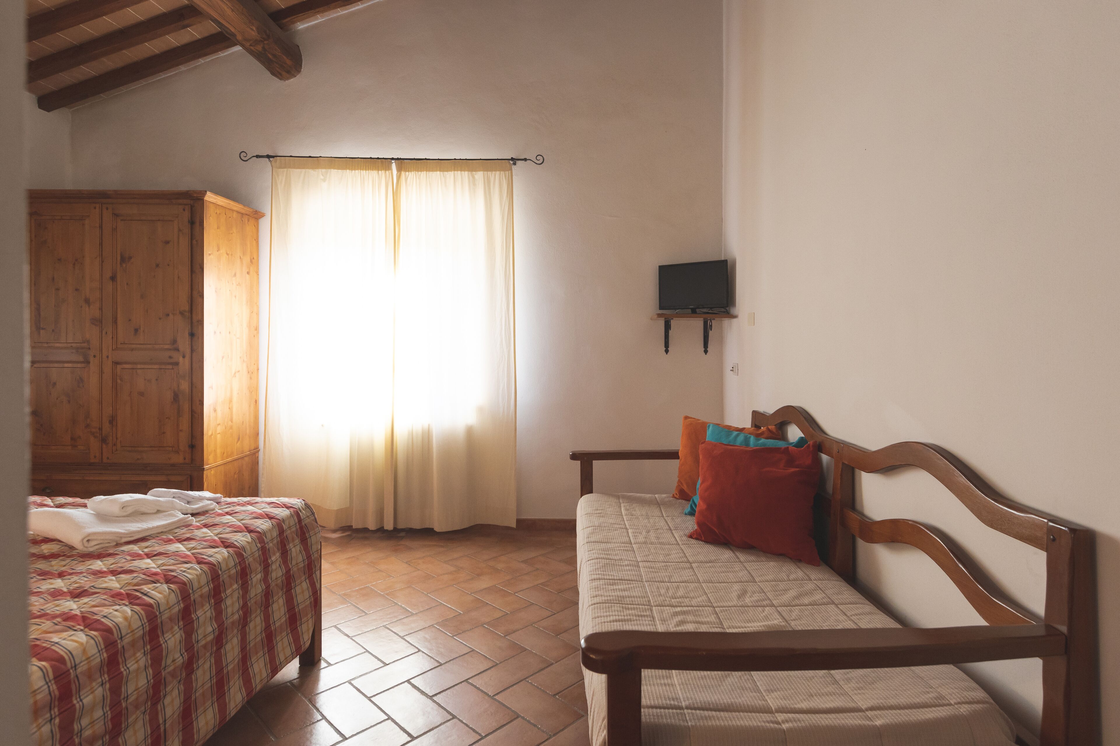 Una camera da letto con due letti, un armadio in legno, una televisione a muro e una finestra con tende.