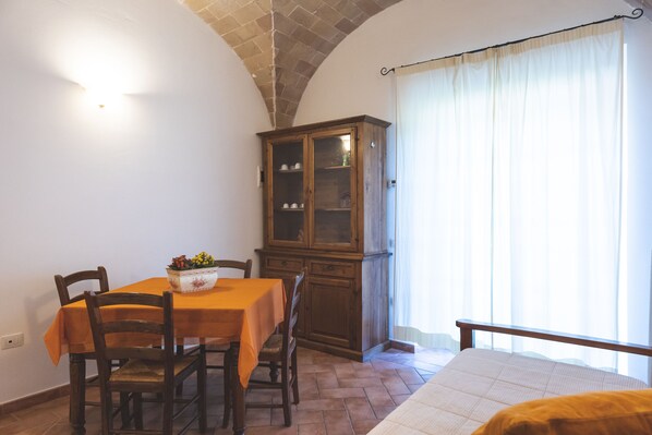 Una zona de comedor con una mesa preparada para dos personas, un aparador de madera y una cama con cabecero.