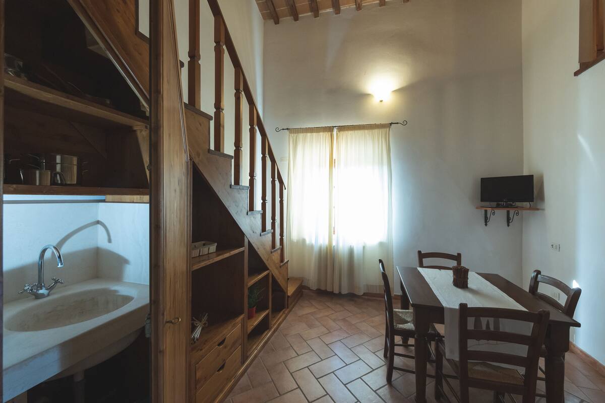 A kitchen with a wooden staircase, a sink, and a dining table with chairs.