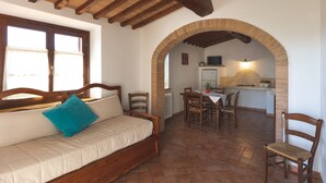 A cozy room with a wooden bed, a dining area, and an archway leading to a kitchen. - Resort Le Tegole (Riparbella)