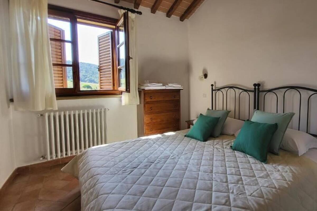 A bedroom with a bed, wooden dresser, and a window with curtains.