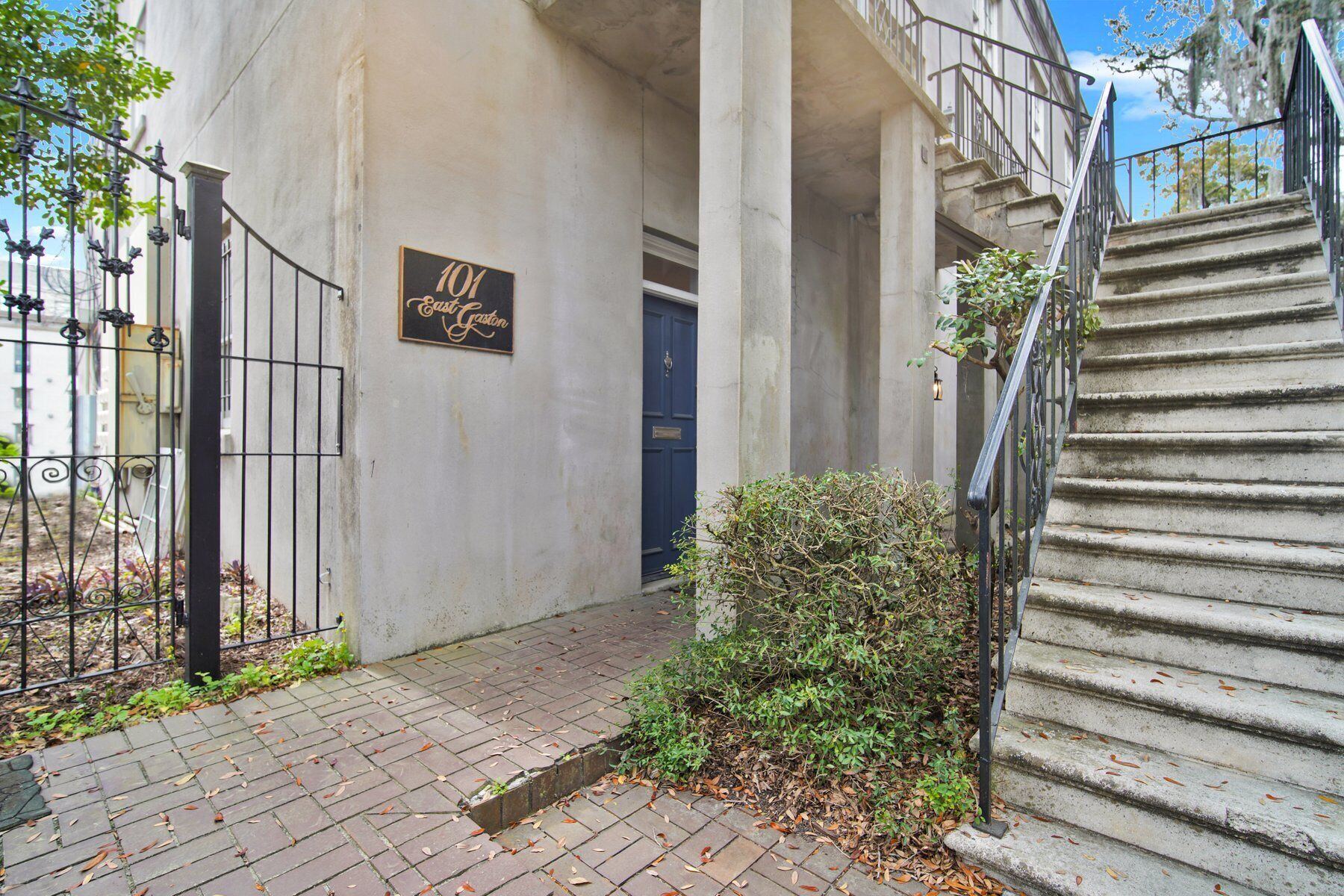 A building entrance with a sign reading "101 East Garden," a blue door, a metal gate, and a concrete staircase.