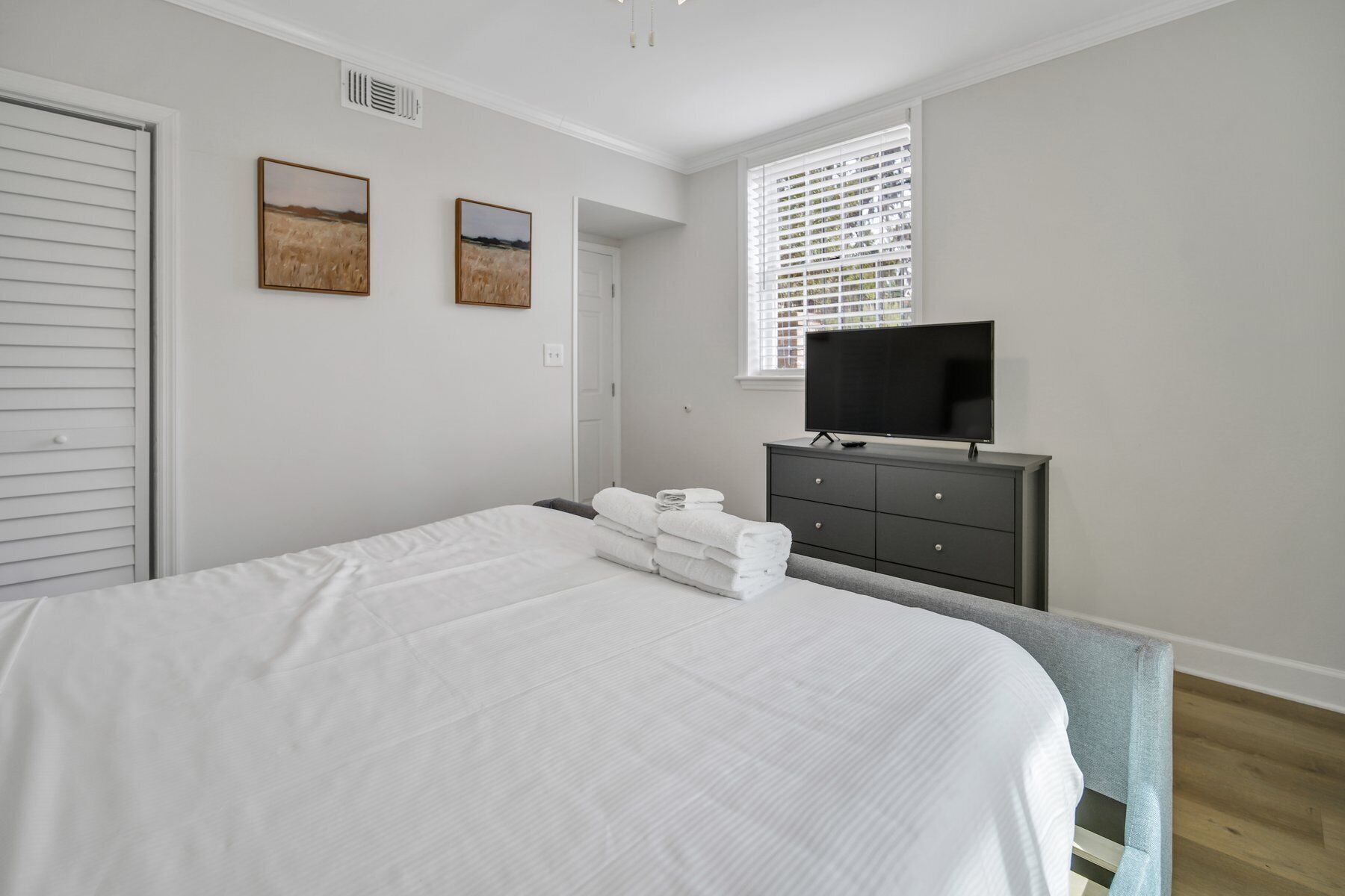 Un dormitorio con una cama, un televisor sobre un tocador y dos cuadros en la pared.