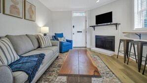 Ein Wohnzimmer mit Sofa, blauem Sessel, Couchtisch, Kamin, Fernseher und einem gemusterten Teppich.