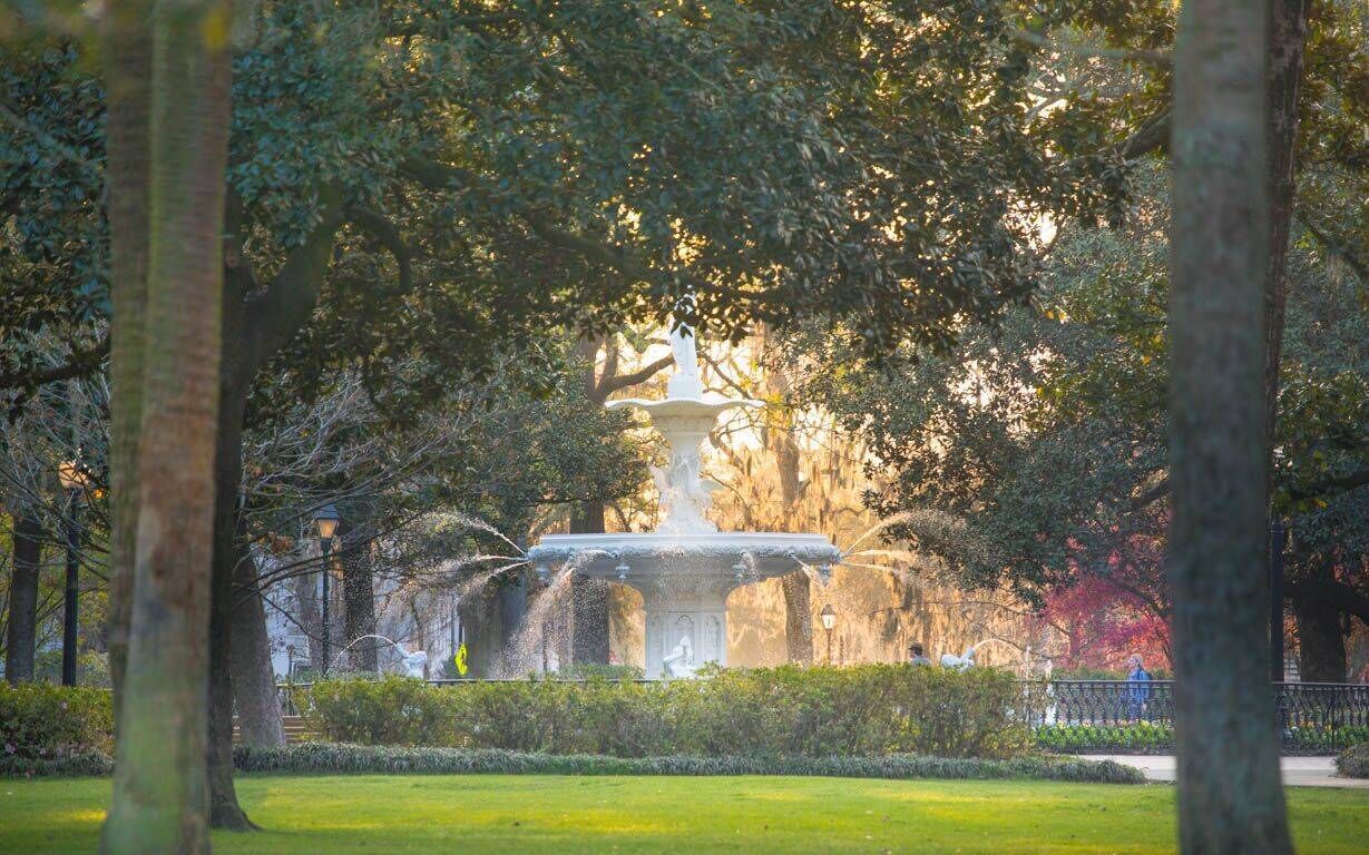 Uma fonte em um parque com árvores e uma estátua.