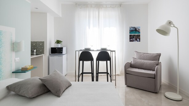 A modern, minimalist room with a bed, a desk with two chairs, a sofa, and a floor lamp.