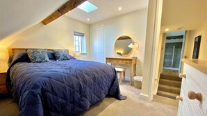 A bedroom with a large bed, a dresser, a mirror, and a staircase leading to another level. - Tilly's Perfect Apartment in charming Ledbury (Ledbury)