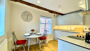 A modern kitchen with white cabinets, a central island, and a dining area with two chairs and a table. - Tilly's Perfect Apartment in charming Ledbury (Ledbury)