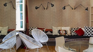 A modern living room with a sofa, two white wireframe chairs, a glass coffee table, and a bookshelf. - Sui Tetti del Centro di Genova by Wonderful Italy (Genova)