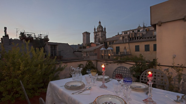 An outdoor dining table set with dinnerware, glasses, and candles, overlooking a cityscape with historic buildings. - Sui Tetti del Centro di Genova by Wonderful Italy (Genova)