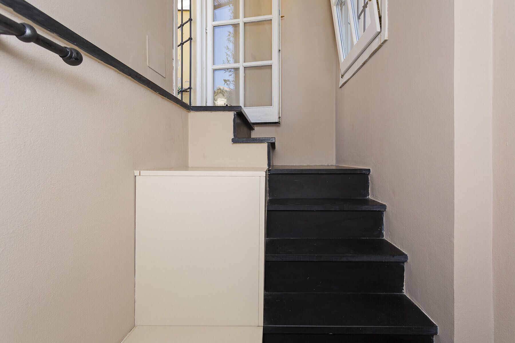 Una escalera con escalones negros y una pared color beige.