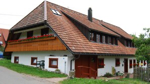 Ein traditionelles Chalet mit geneigtem Dach, Holzbalkon und kleiner Veranda.