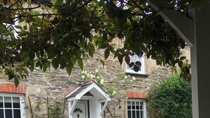 An outdoor patio with a stone wall, white door, and a small white building with a sign reading "Jam Mr." - Beautiful Cottage close to the beach w/ sunny garden (Crantock)