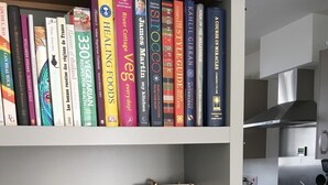 A bookshelf with various books, a 'LOVE' sign, decorative items, and a kitchen in the background. - Beautiful Cottage close to the beach w/ sunny garden (Crantock)