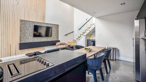 Eine moderne Küche mit integrierter Kochinsel, einem Flachbildfernseher und einer Treppe, die in ein Obergeschoss führt.