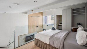 A modern bedroom with a bed, a built-in fireplace, a glass partition, and a view of the outside.