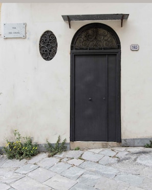 A black door with a metal decorative arch above it, a sign reading "VIA DEL CELSO", and a house number "145".