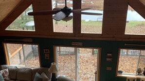 Spazioso loft con soffitto alto, ampie finestre, ventilatore a soffitto, divano componibile, tavolo da pranzo e vista su una zona boschiva.
