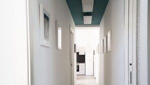 Un corridoio stretto con pareti bianche, un soffitto color acquamarina e una cucina visibile in fondo.