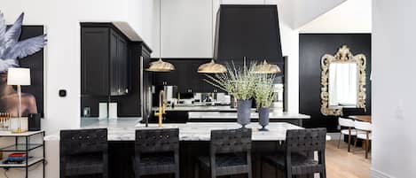 A modern kitchen with black cabinets, a marble island, and pendant lighting.