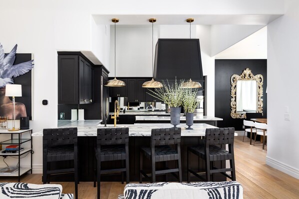 Una cocina moderna con gabinetes negros, una isla de mármol e iluminación colgante.