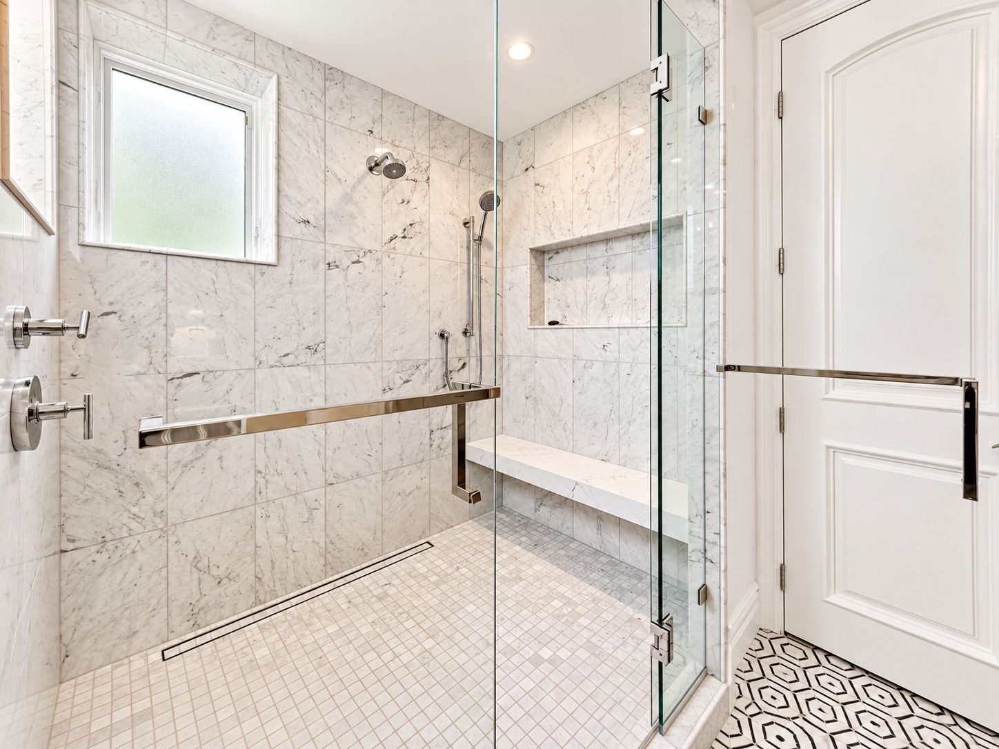 Une salle de bain moderne avec une douche à parois de verre, des murs en marbre et une porte blanche.
