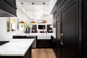 Una cocina moderna con armarios oscuros, encimera de mármol e iluminación colgante.