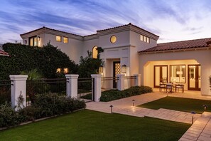 Una casa moderna de dos pisos con un césped bien cuidado, un acceso con portón y un patio con mobiliario exterior.