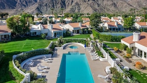 Een resort met een centraal gelegen zwembad, meerdere villa’s en een bergachtig landschap op de achtergrond.