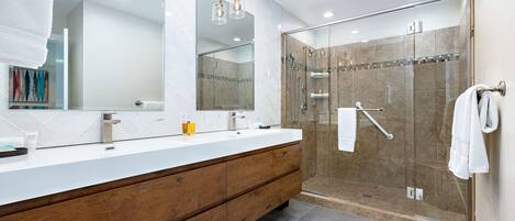 A modern bathroom with a white vanity, wooden cabinets, a glass shower enclosure, and a large mirror.