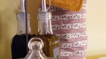 A kitchen counter with a jar of flour, two bottles of olive oil, and a yellow towel hanging on a patterned cloth.