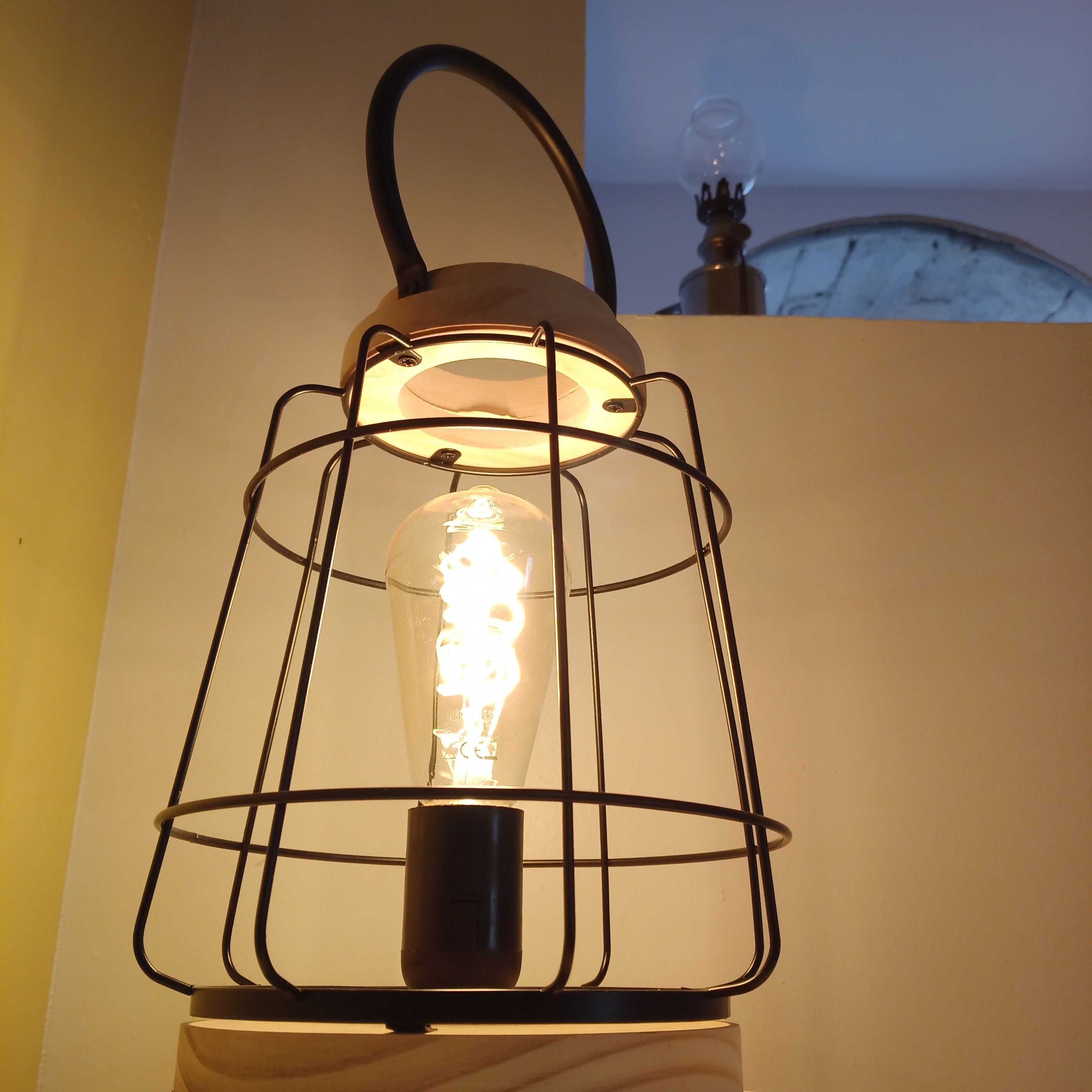 A metal lantern with a visible filament bulb, mounted on a white base.
