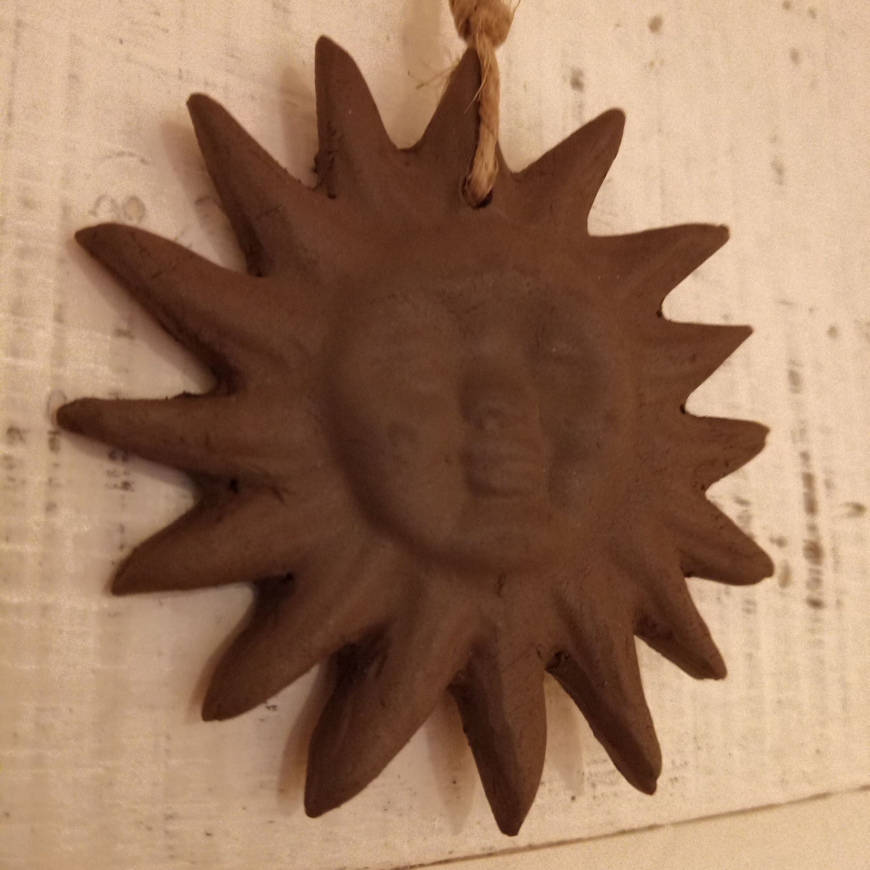 Aurinkoa muistuttava koriste, jonka keskellä on kasvot, ja se on ripustettu kuvioituun pintaan.