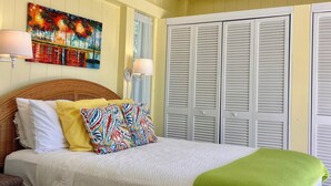 Una cama bien hecha con un plaid verde, un cuadro colorido en la pared y una ventana con contraventanas.