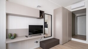 A modern living room with a flat-screen TV, a built-in shelf with decorative items, a bench, and a large mirror.
