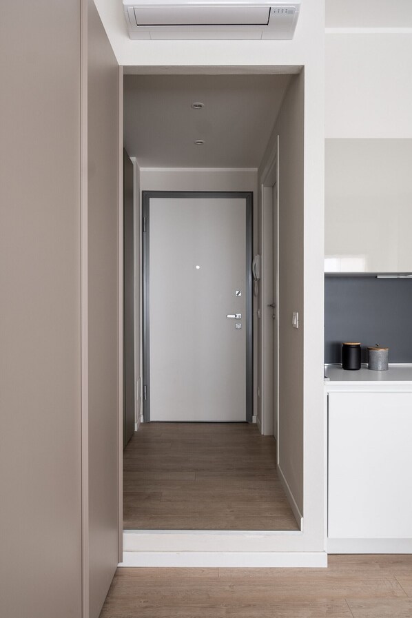 Un couloir étroit mène à une porte. Sur le côté droit, on trouve un espace cuisine moderne, avec un plan de travail et deux récipients.
